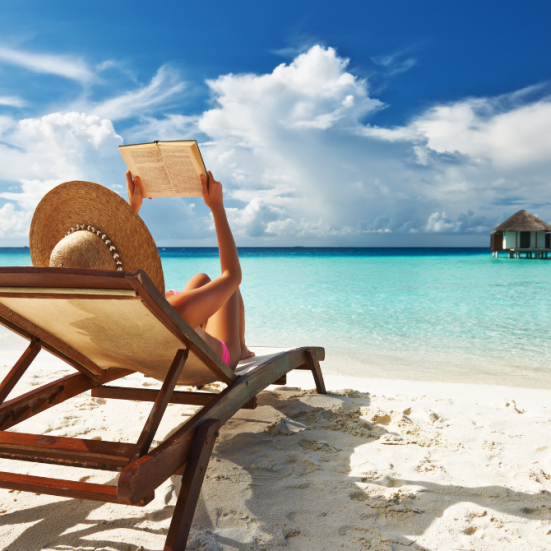 Kvinde med bog i liggestol på strand