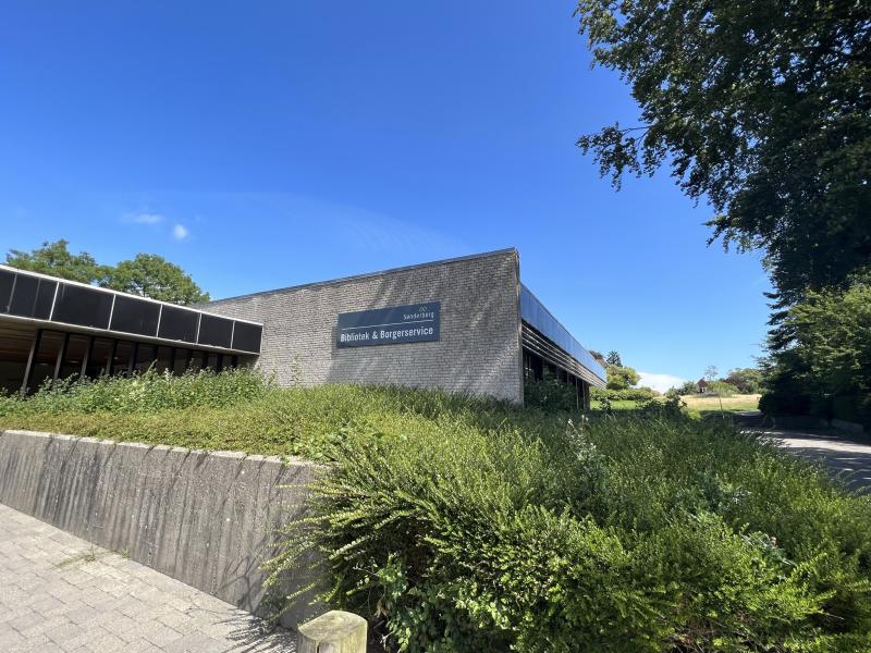 Biblioteket i Nordborg ses forfra. Der er træer og planter i forgrunden.
