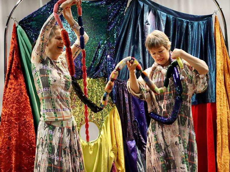 To kvindelige skuespillere i en farverig kulisser med forskellige ruller af farvet stof.