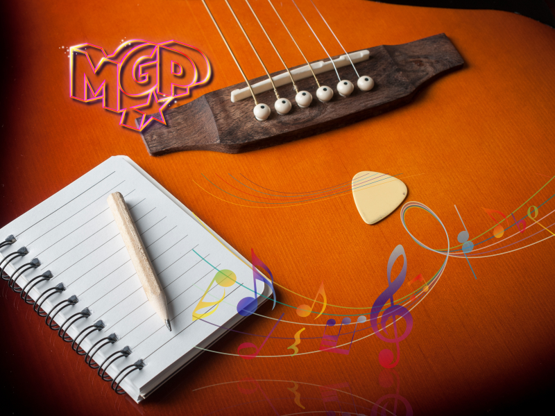 En guitar hvorpå der ligger en linjeret blok og en blyant. På guitaren er der også indsat noder i forskellige farver.